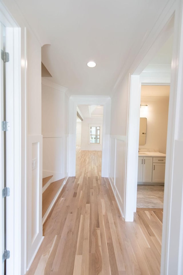 hallway with a wainscoted wall, ornamental molding, a decorative wall, and light wood finished floors