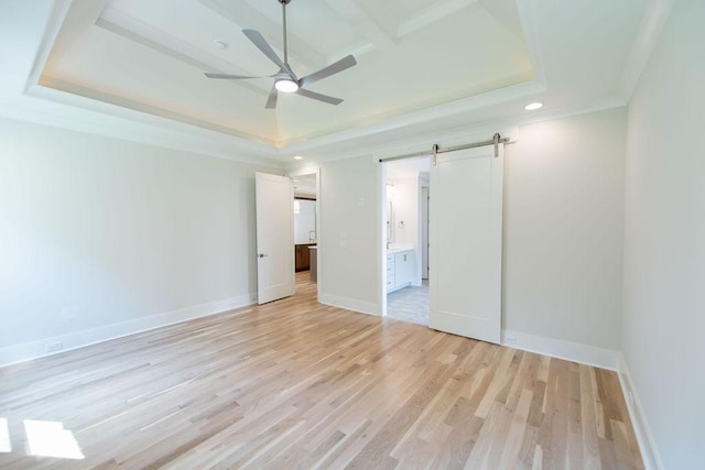 unfurnished bedroom featuring light wood-style flooring, a tray ceiling, recessed lighting, and a barn door