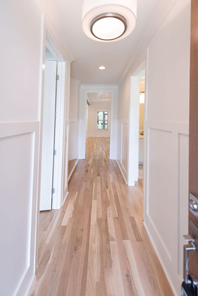 hall with a wainscoted wall, a decorative wall, and light wood-style flooring