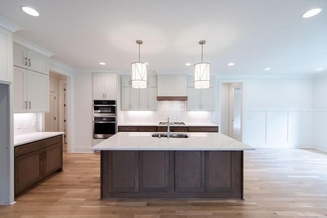 kitchen featuring stainless steel double oven, tasteful backsplash, a sink, light wood-style floors, and white cabinetry