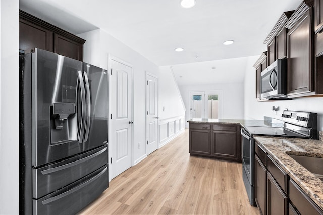kitchen with appliances with stainless steel finishes, dark brown cabinets, light stone counters, a peninsula, and light wood finished floors