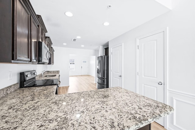 kitchen with dark brown cabinetry, appliances with stainless steel finishes, light stone countertops, a sink, and light wood finished floors