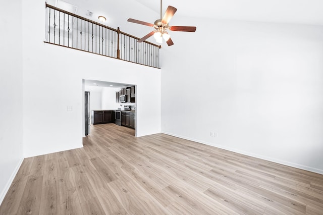 unfurnished living room featuring light wood-style floors, baseboards, ceiling fan, and a towering ceiling