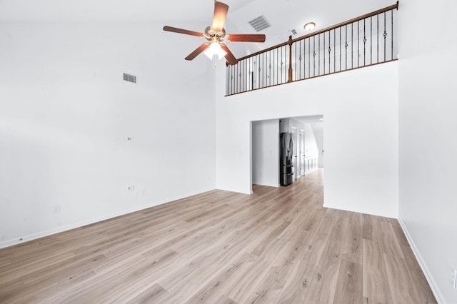 unfurnished living room with visible vents, a ceiling fan, light wood-style floors, and a high ceiling