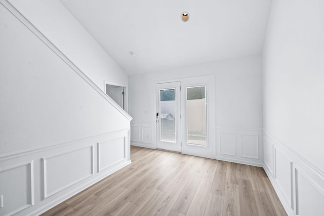 empty room featuring lofted ceiling, wainscoting, light wood finished floors, and a decorative wall