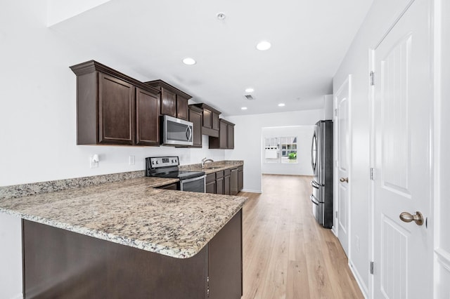 kitchen with dark brown cabinetry, appliances with stainless steel finishes, light stone countertops, a sink, and light wood-style flooring