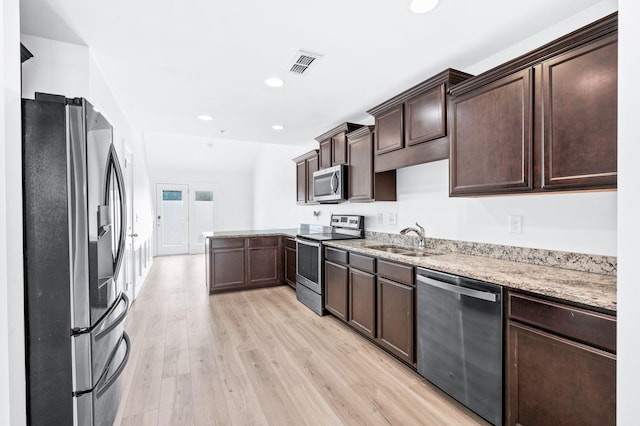 kitchen featuring dark brown cabinetry, light stone countertops, a sink, stainless steel appliances, and light wood-style flooring