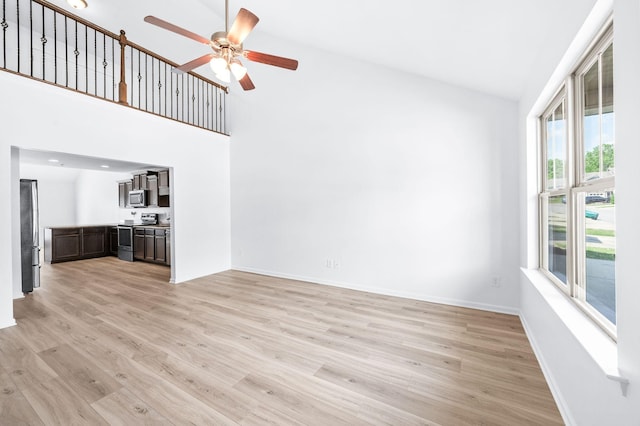 unfurnished living room featuring baseboards, ceiling fan, light wood-style flooring, and a high ceiling