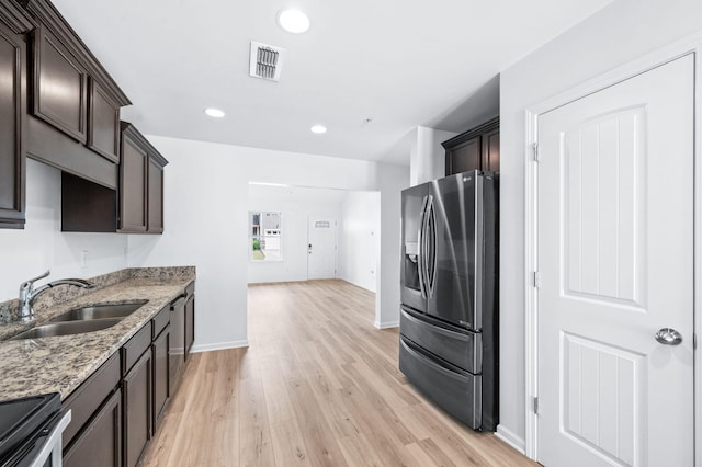 kitchen featuring dark brown cabinetry, light stone countertops, light wood-type flooring, a sink, and stainless steel appliances
