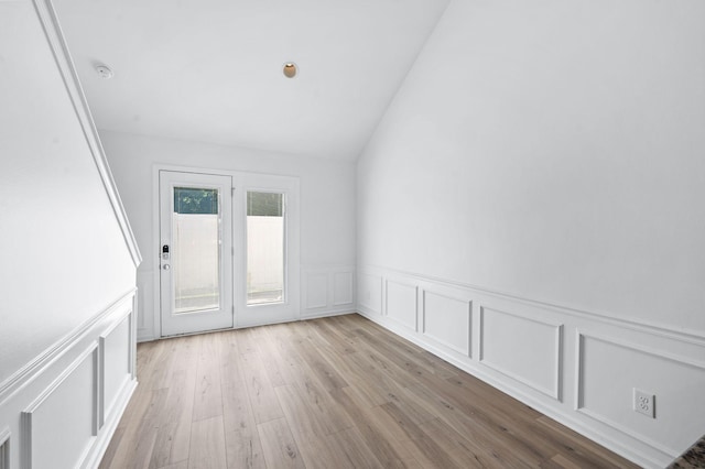 unfurnished room featuring light wood-style floors, wainscoting, lofted ceiling, and a decorative wall