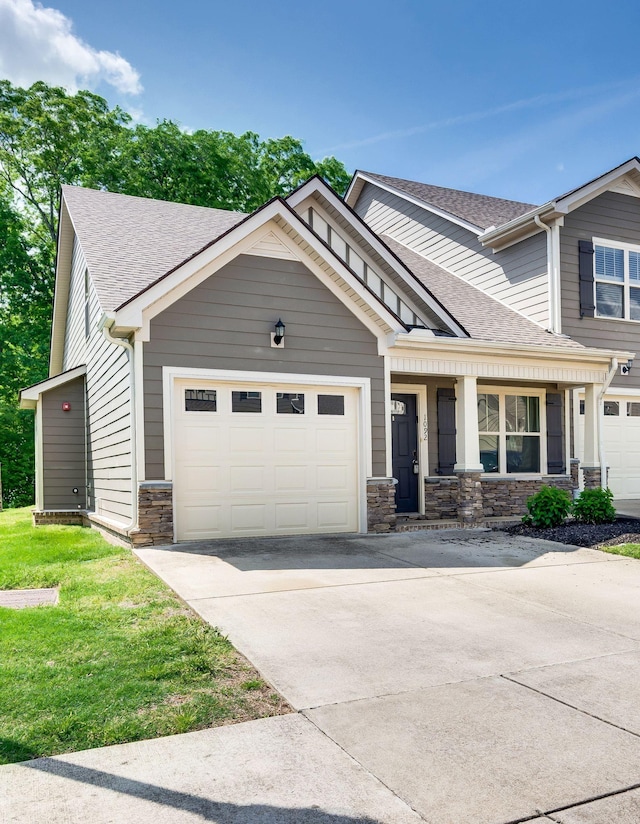 craftsman-style house featuring covered porch, concrete driveway, an attached garage, a shingled roof, and stone siding