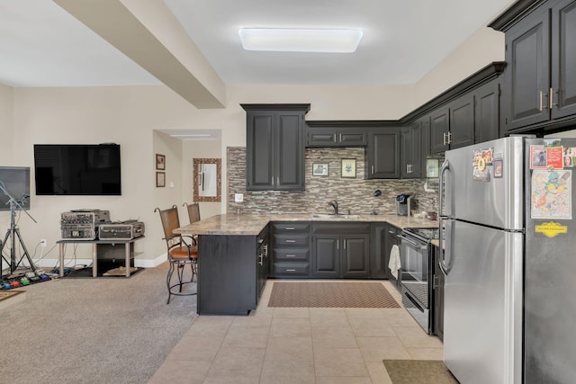 kitchen with electric range, a sink, freestanding refrigerator, a peninsula, and backsplash