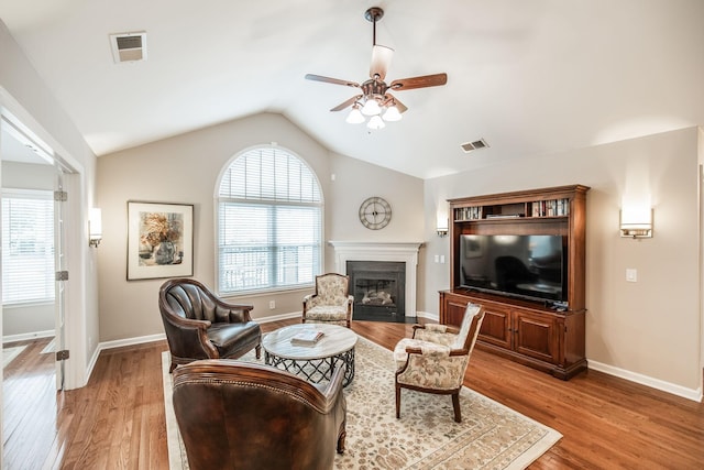 living area featuring visible vents, a ceiling fan, a glass covered fireplace, and light wood-type flooring
