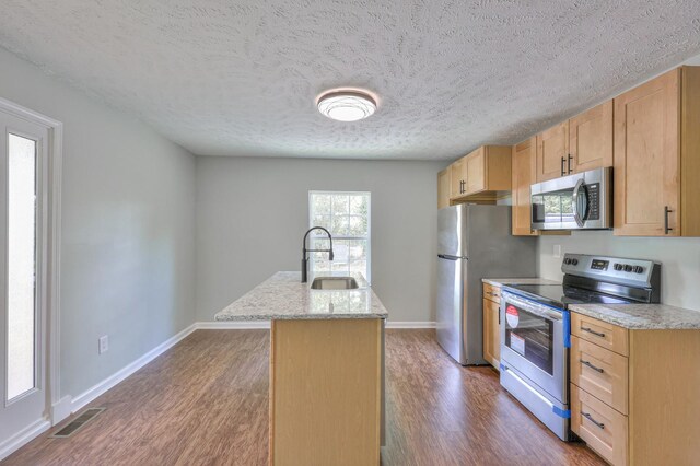 kitchen featuring appliances with stainless steel finishes, a sink, an island with sink, wood finished floors, and visible vents