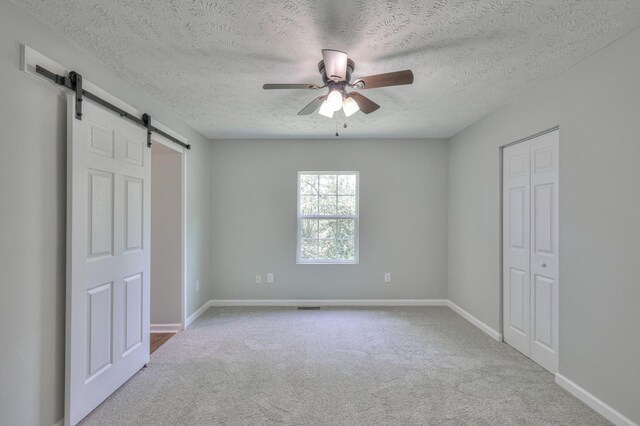 unfurnished bedroom featuring carpet flooring, a textured ceiling, a barn door, and baseboards
