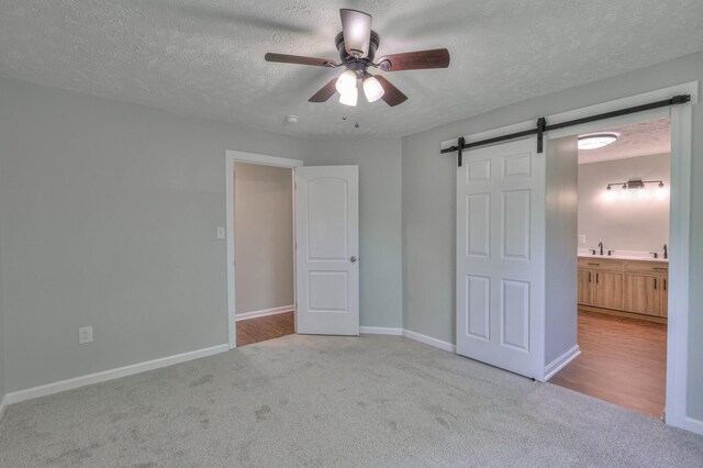 unfurnished bedroom with a barn door, a sink, carpet floors, a textured ceiling, and baseboards