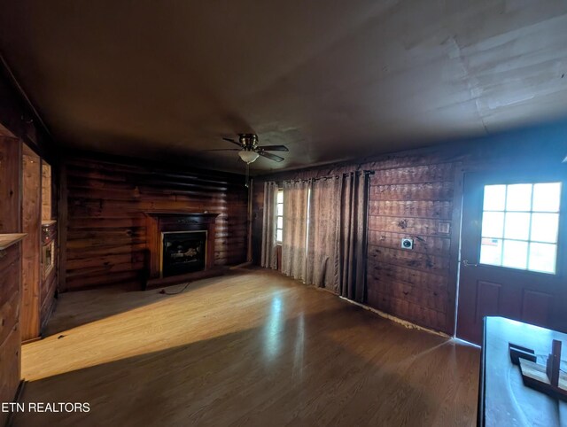unfurnished living room with ceiling fan, a fireplace with raised hearth, and wood finished floors
