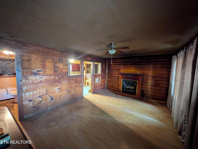 unfurnished living room featuring ceiling fan, wood finished floors, wooden walls, and a fireplace