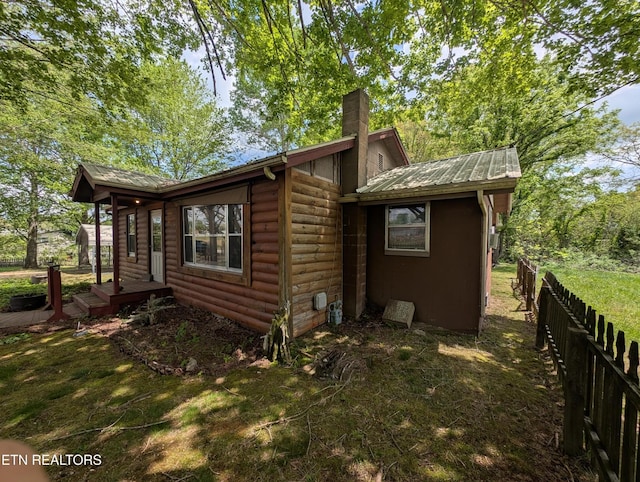 view of property exterior with fence, faux log siding, a chimney, and metal roof