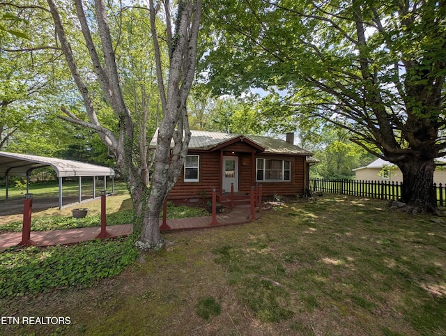 exterior space featuring a chimney, a carport, faux log siding, fence, and a yard
