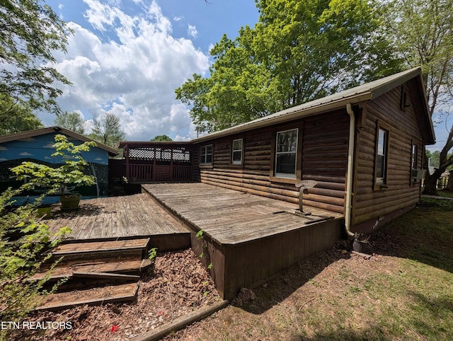 back of property with faux log siding and a deck