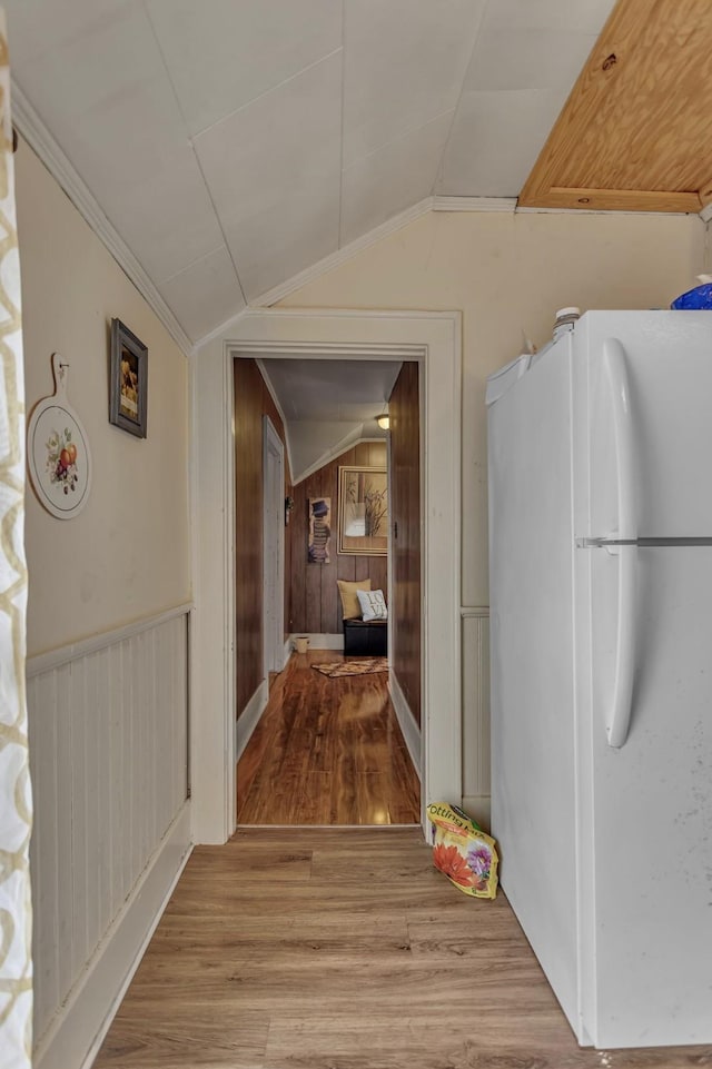 hallway with wooden walls, vaulted ceiling, ornamental molding, and wood finished floors