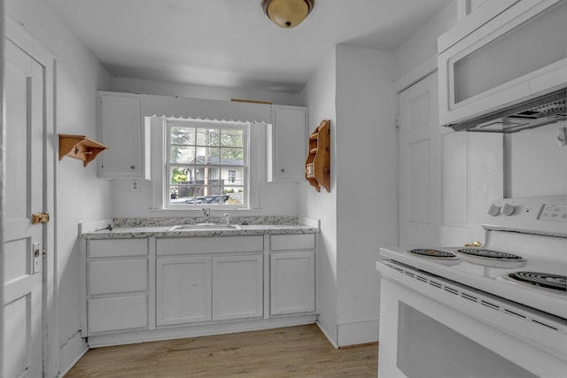 kitchen featuring white appliances, white cabinets, light stone counters, a sink, and light wood finished floors