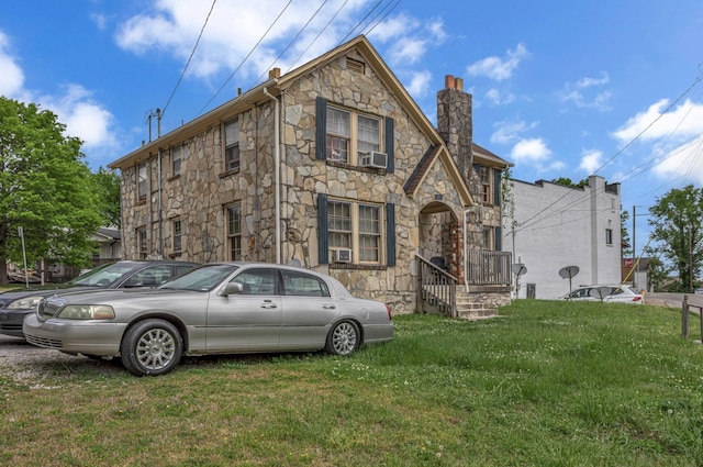 english style home with a chimney, stone siding, and a front lawn