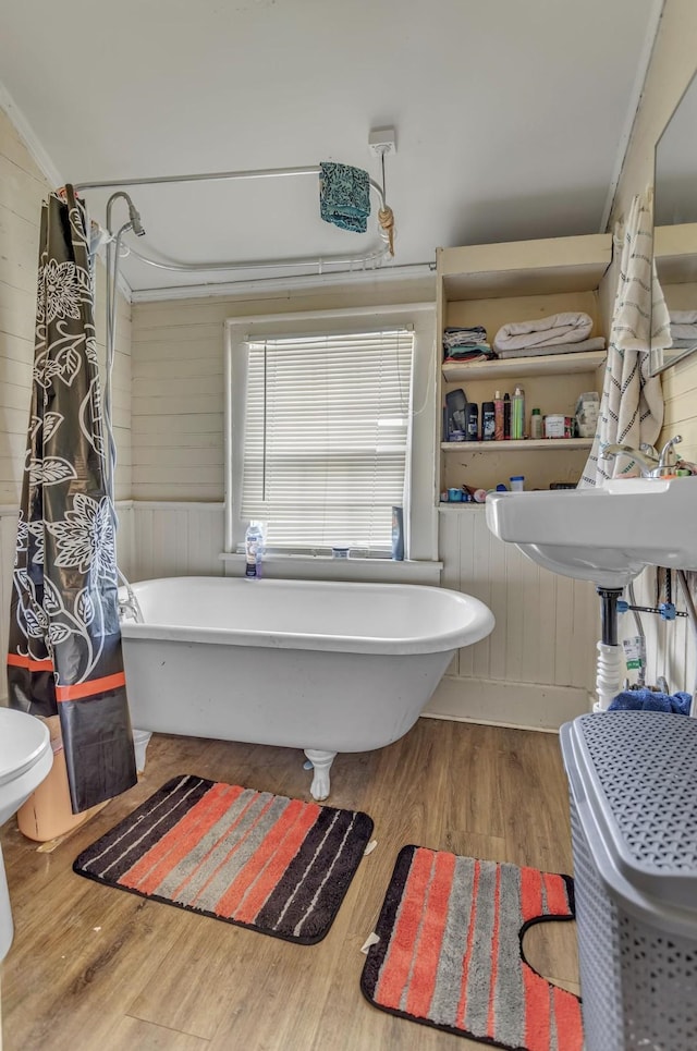 bathroom with wooden walls, a freestanding bath, toilet, a shower with shower curtain, and wood finished floors