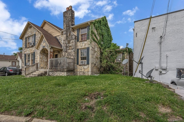 tudor-style house featuring a front yard, a chimney, and stone siding
