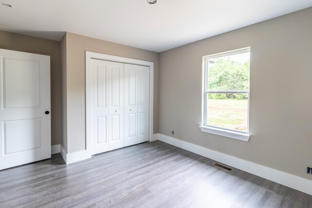 unfurnished bedroom featuring baseboards, visible vents, wood finished floors, and a closet