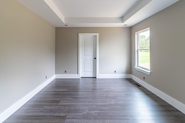 empty room with visible vents, dark wood-style flooring, baseboards, and a tray ceiling