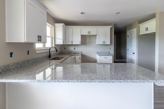 kitchen with a sink, light stone countertops, a peninsula, and white cabinetry