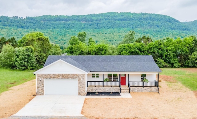 view of front of house with covered porch, a garage, a wooded view, concrete driveway, and a shingled roof