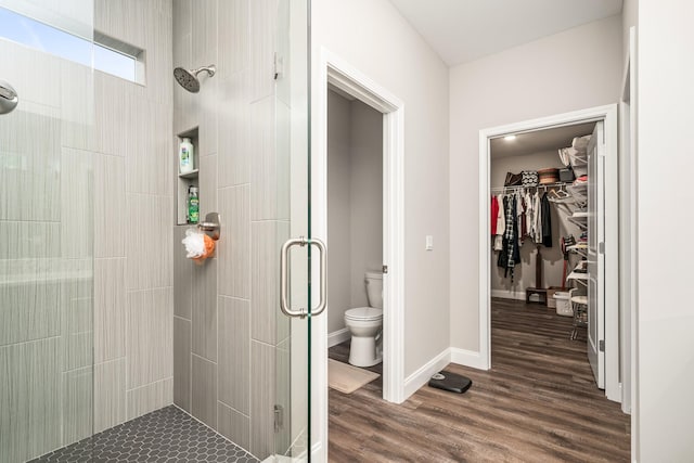 bathroom featuring toilet, a walk in closet, wood finished floors, and a stall shower