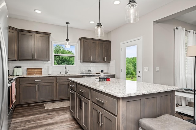 kitchen with dark brown cabinetry, backsplash, dark wood finished floors, a sink, and light stone counters