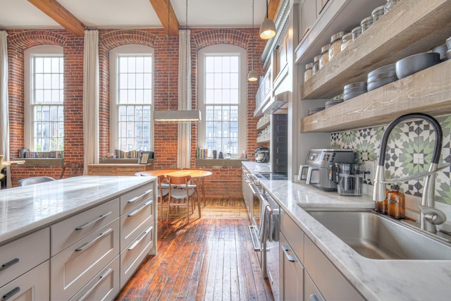 kitchen with open shelves, beam ceiling, a sink, brick wall, and hardwood / wood-style flooring