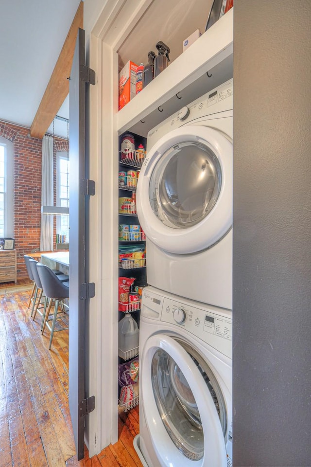 clothes washing area featuring wood-type flooring, laundry area, and stacked washing maching and dryer