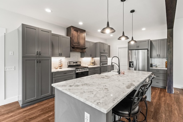kitchen with appliances with stainless steel finishes, a sink, a kitchen breakfast bar, gray cabinets, and decorative backsplash