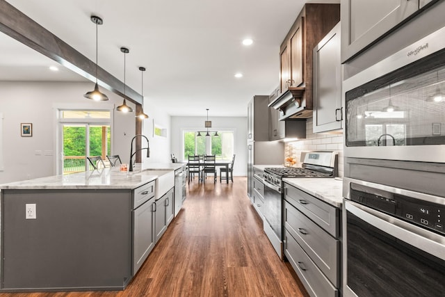 kitchen with a sink, stainless steel appliances, a large island with sink, gray cabinetry, and dark wood-style floors