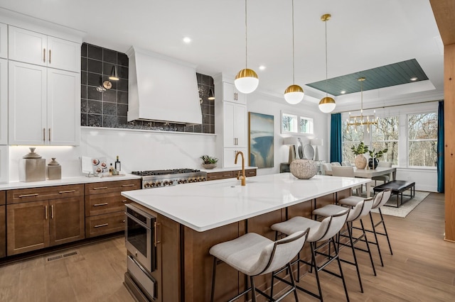 7258 Murrel Dr, Franklin, TN 37064 - kitchen featuring a breakfast bar area, wall chimney exhaust hood, white cabinets, a sink, and light wood finished floors