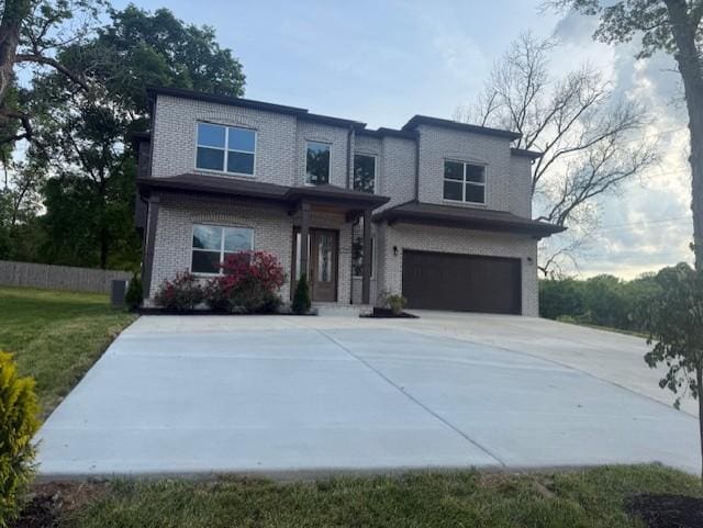 view of front of house with an attached garage, concrete driveway, a front yard, and brick siding