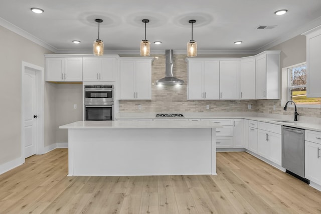 kitchen with ornamental molding, wall chimney range hood, light countertops, a sink, and stainless steel appliances