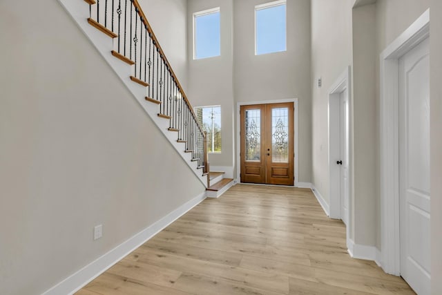 foyer featuring stairs, baseboards, a high ceiling, arched walkways, and light wood finished floors
