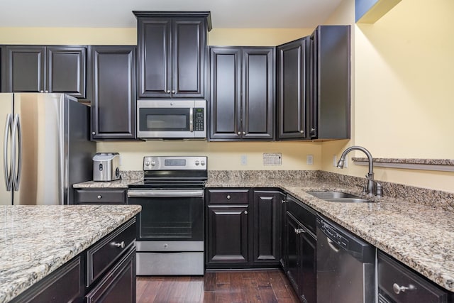 kitchen with appliances with stainless steel finishes, light stone countertops, dark wood finished floors, a sink, and dark cabinetry