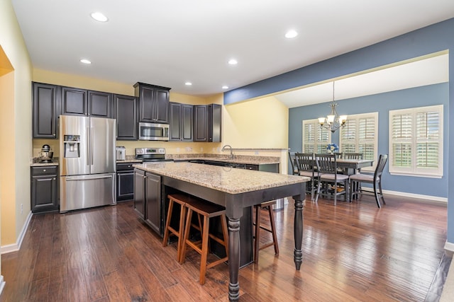 kitchen with appliances with stainless steel finishes, a breakfast bar, an inviting chandelier, baseboards, and a kitchen island