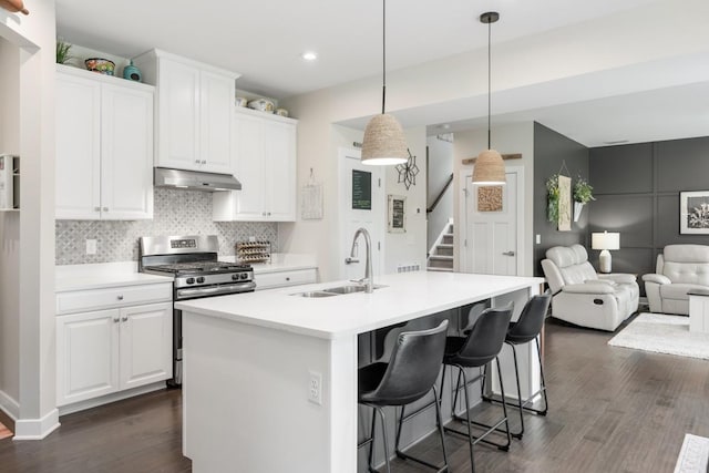 kitchen with a sink, stainless steel gas range oven, dark wood finished floors, open floor plan, and under cabinet range hood