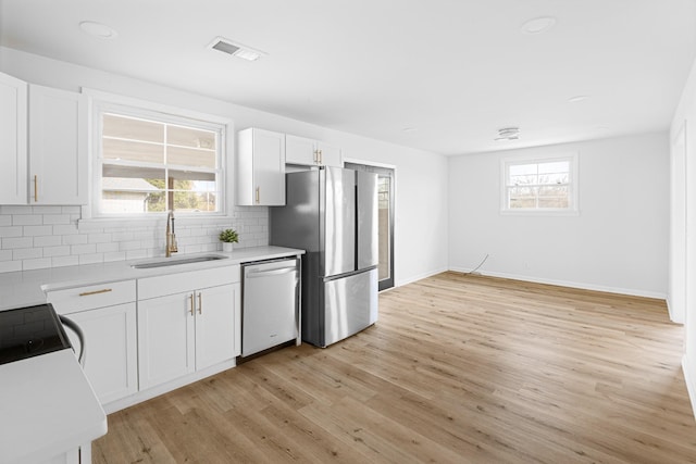 kitchen with decorative backsplash, light countertops, a sink, light wood finished floors, and dishwashing machine