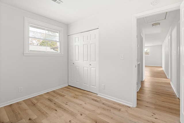 unfurnished bedroom featuring visible vents, a closet, light wood-style floors, attic access, and baseboards