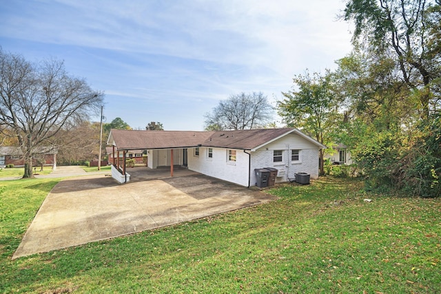 rear view of house with brick siding, an attached carport, central AC unit, concrete driveway, and a yard
